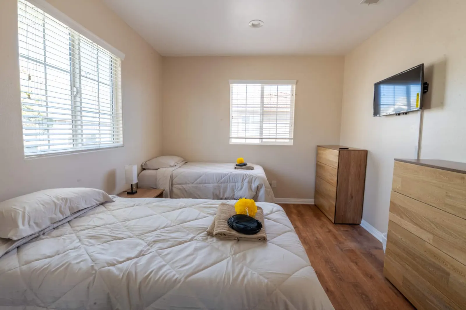 Bedroom with two beds, a tall wooden dresser, and a wall-mounted television