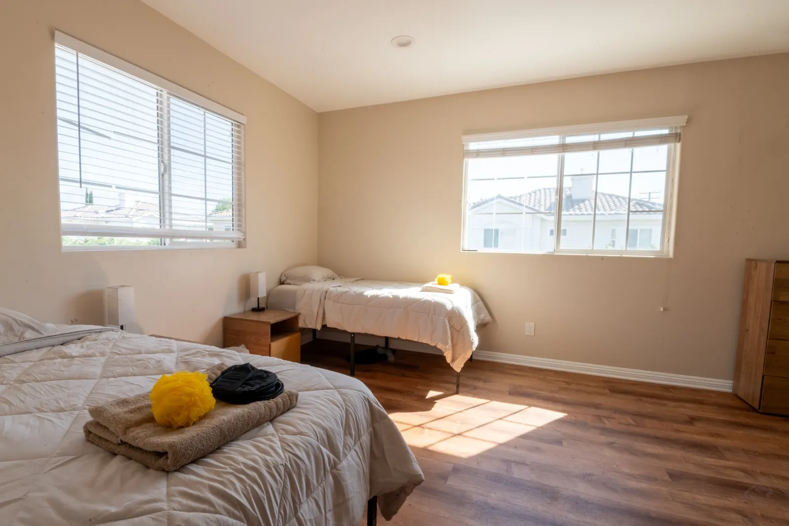 Sunlit bedroom with two beds and a bedside table between the windows